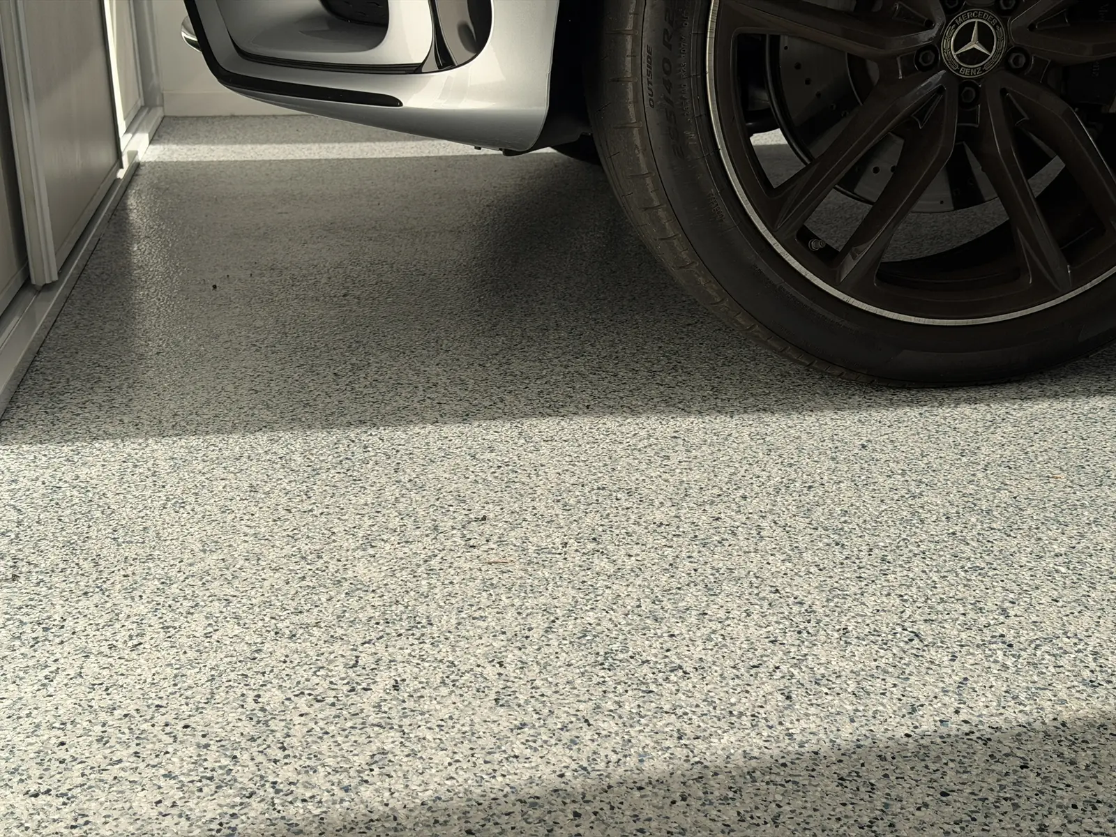 Grey decorative flake garage floor shown beside a parked vehicle